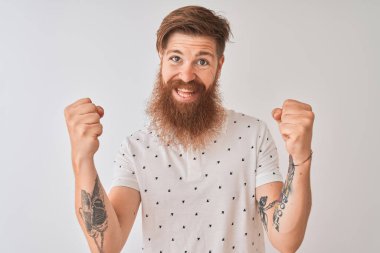 İzole beyaz arka plan üzerinde Polo ayakta giyen genç Redhead İrlandalı adam şaşırttı ve silah kaldırdı ve açık gözleri ile başarı için hayran kutluyor. Kazanan kavramı.