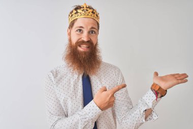El ile sunmak ve parmak ile işaret ederken genç Redhead İrlandalı işadamı izole beyaz arka plan hayran ve kameraya gülümseyen üzerinde taç kral giyiyor.