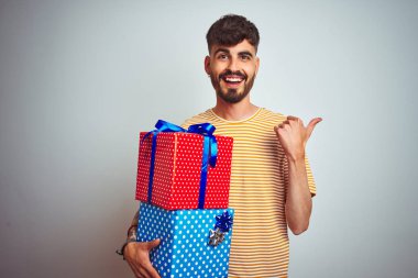 Dövme tutan genç adam izole beyaz arka plan üzerinde ayakta Doğum günü hediyeleri duran ve mutlu yüz gülümseyen yan başparmak ile gösteren