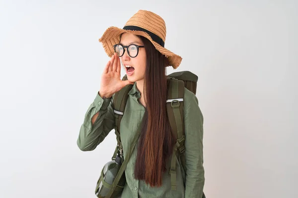 Chinese hiker woman wearing canteen hat glasses backpack over isolated white background shouting and screaming loud to side with hand on mouth. Communication concept.