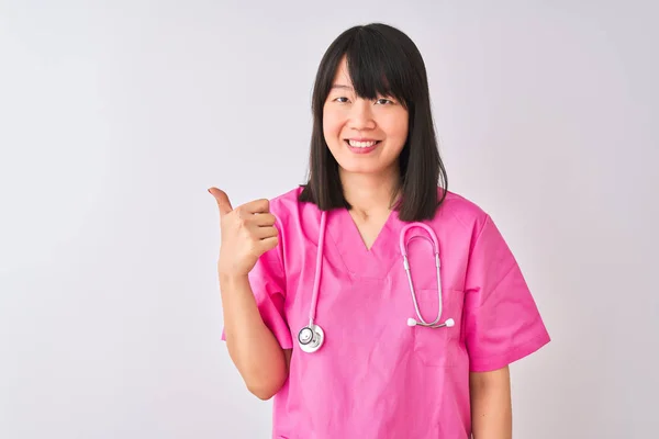年轻漂亮的中国护士妇女穿着听诊器在孤立的白色背景做快乐竖起大拇指手势与手 批准显示显示成功的相机的表达式 — 图库照片