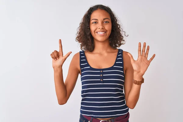 孤立した白い背景の上に立つストライプのTシャツを着た若いブラジル人女性は 自信を持って幸せに微笑みながら 指番号7を示し 指を上げている — ストック写真