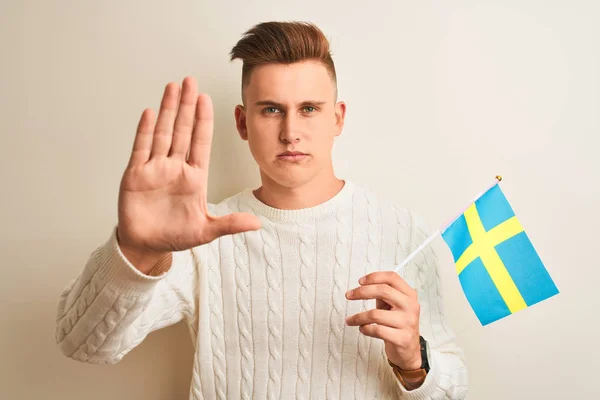 孤立した白い背景の上にスウェーデンの旗を持つ若いハンサムな男は 真剣で自信に満ちた表情でストップサインを行い 防衛ジェスチャー — ストック写真