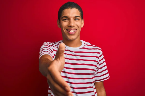 年轻的英俊的阿拉伯男子穿着条纹T恤在孤立的红色背景微笑友好提供握手作为问候和欢迎 成功的业务 — 图库照片