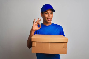 Genç yakışıklı arap teslimat adam parmakları, mükemmel sembolü ile ok işareti yapıyor izole beyaz arka plan üzerinde duran bir kutu tutan