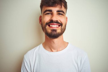 Dövme ile genç adam yüz üzerinde mutlu ve serin bir gülümseme ile izole beyaz arka plan üzerinde ayakta tişört giyiyor. Şanslı kişi.