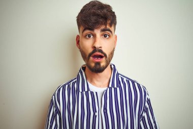 İzole beyaz arka plan üzerinde ayakta çizgili gömlek giyen dövme ile genç adam korkuyor ve sürpriz ifade, korku ve heyecanlı yüz ile şok.