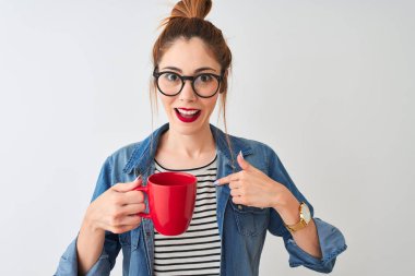 Genç, güzel, kızıl saçlı bir kadın izole edilmiş beyaz arka planda bir fincan kahve içiyor.