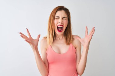 İzole beyaz arka plan üzerinde ayakta rahat pembe t-shirt giyen güzel kızıl saçlı kadın çılgın ve deli çığlık ve agresif ifade ve silah ile bağırdı kaldırdı. Hayal kırıklığı kavramı.