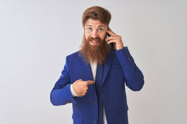 Genç Redhead İrlandalı işadamı kendini sürpriz yüz işaret parmak ile izole beyaz arka plan üzerinde Smartphone konuşuyor