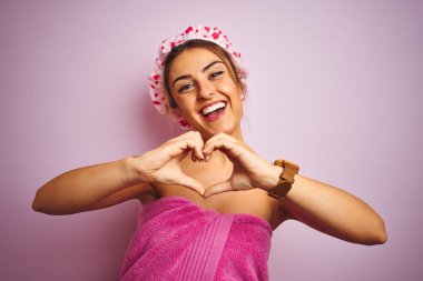 Genç güzel kadın havlu giyen ve izole pembe arka plan üzerinde duş kapağı sevgi gösteren kalp sembolü ve el ile şekil gülümseyen. Romantik konsept.