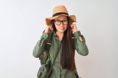 Çinli otostopçu kadın yüksek sesle müzik gürültü için rahatsız ifade ile parmaklar ile izole beyaz arka plan üzerinde kantin şapka gözlük sırt çantası giyiyor. Sağır kavramı.