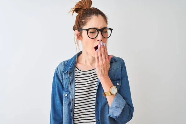 Redhead woman wearing striped t-shirt denim shirt and glasses over isolated white background bored yawning tired covering mouth with hand. Restless and sleepiness.