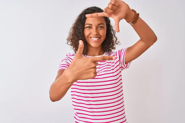 ピンクのストライプのTシャツを着た若いブラジル人女性は 孤立した白い背景の上に立って 幸せそうな顔で手と指でフレームを作って微笑んでいます 創造性と写真のコンセプト — ストック写真