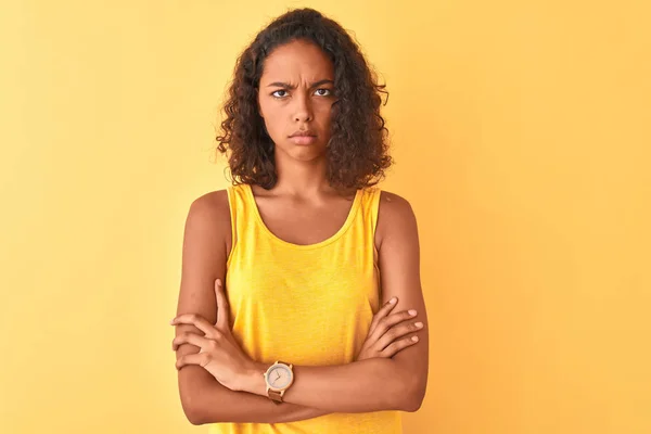 Young brazilian woman wearing t-shirt standing over isolated yellow background skeptic and nervous, disapproving expression on face with crossed arms. Negative person.