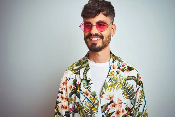 Man with tattoo on vacation wearing summer shirt sunglasses over isolated white background looking away to side with smile on face, natural expression. Laughing confident.