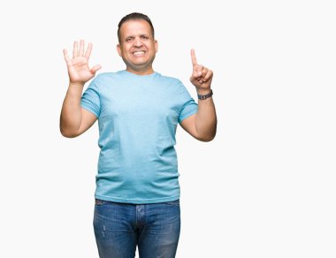 Orta yaş Arap adam üzerinde gösterilen ve parmakları ile işaret izole arka plan mavi t-shirt giyen süre kendinden emin ve mutlu gülümseyerek 6 numara.