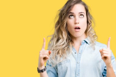 İzole arka plan üzerinde sarışın güzel genç kadın hayrete ve yukarıya bakıyor ve parmakları ile işaret ve silah kaldırdı şaşırttı.