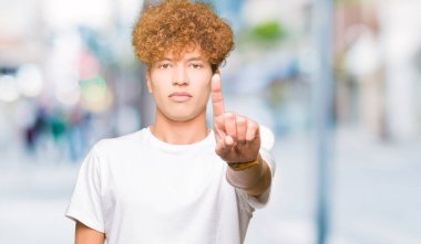 Yakışıklı delikanlı afro saçlı kadar rahat beyaz t-shirt işaret parmağınızla giyen ve kızgın ifade
