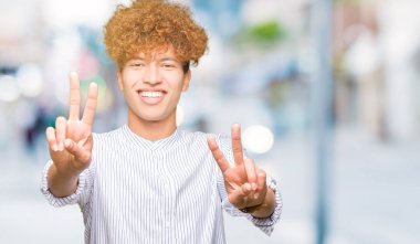 Genç yakışıklı iş adamı zafer işareti yapıyor parmak gösterilen kamera seyir gülümseyen afro saç giyen şık gömlek ile. İki numaralı.
