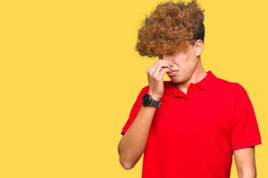 Afro saç ile genç yakışıklı adam kırmızı t-shirt kokusu bir şey kokmuş ve mide bulandırıcı, dayanılmaz koku, burun parmaklar ile nefes tutan giyiyor. Kötü koku kavramı.