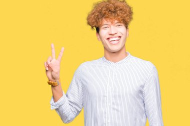 Afro saç ile genç yakışıklı iş adamı zarif gömlek gülümseyen mutlu yüz ile fotoğraf makinesi zafer işareti yapıyor göz kırpıyor. İki numara.