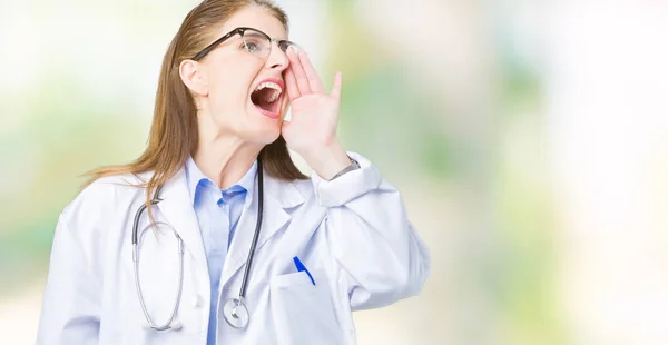 中年成熟的医生妇女穿着医疗外套在孤立的背景下大喊大叫 大声尖叫着一边 手放在嘴边 沟通理念 — 图库照片