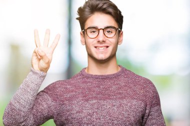 Gösterilen arka plan üzerinde gözlük takan genç yakışıklı adam izole ve parmakları ile işaret üçüncü gülümseyen ise kendinden emin ve mutlu.