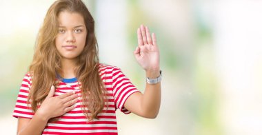 Giyen genç güzel esmer kadın çizgili tişört izole arka plan üzerinde göğüs ve bir sadakat sözü yemin yapma avuç, el ile küfür