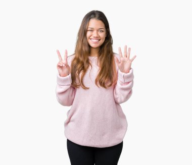 Gösterilen ve parmakları ile işaret izole arka plan üzerinde pembe kış kazak giyen genç güzel esmer kadın kendinden emin ve mutlu gülümseyerek süre yedi numara.