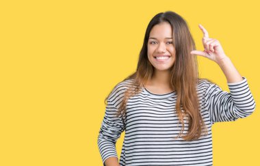 Giyen genç güzel esmer kadın kazak izole arka plan gülümseyen ve süre seyir ve kamera boyutu işaret parmaklarıyla yapıyor el ile kendinden emin eller üzerinde çizgili. Ölçü kavramı.