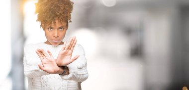 İzole arka plan ret ifade geçiş silah ve avuç içi eksi işareti, kızgın surat yapıyor üzerinde kış kazak giyen güzel genç Afro-Amerikan kadın