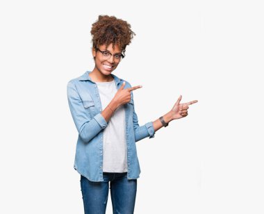 Güzel genç Afro-Amerikan kadın gülümseyerek ve iki elleri ve parmakları ile tarafına işaret kamera bakarak izole arka plan üzerinde gözlük.