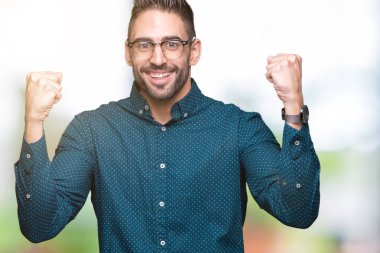 Genç yakışıklı iş adamı izole arka plan üzerinde kutluyor gözlük takan şaşırttı ve başarı için kaldırdı kollarını açarak hayret ve gözleri açık. Kazanan kavramı.