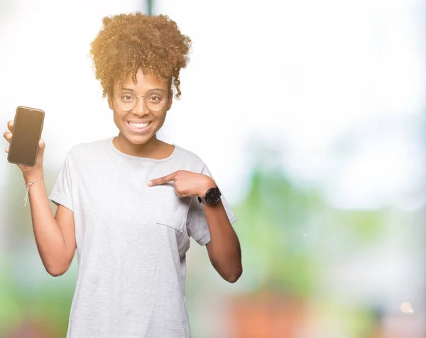 Young african american woman showing smartphone screen over isolated background with surprise face pointing finger to himself