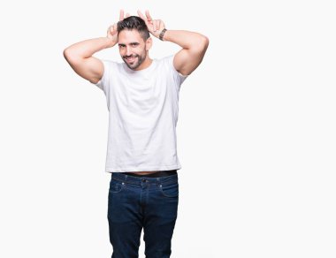 Beyaz izole arka plan üzerinde beyaz t-shirt giyen yakışıklı adam Bunny kulakları olarak kafasına parmaklar ile komik ve deli poz, neşeli gülümseyen