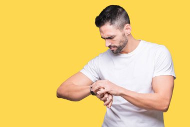 Sarı izole arka planda beyaz t-shirt giyen yakışıklı adam bilek saatindeki saati kontrol etme, rahat ve emin