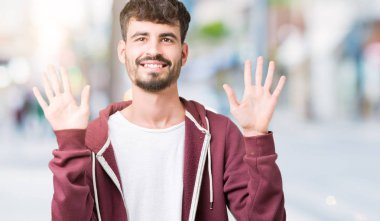 Yakışıklı delikanlı gösterilen ve parmakları ile işaret izole arka plan üzerinde kendinden emin ve mutlu gülümseyerek süre on numara.