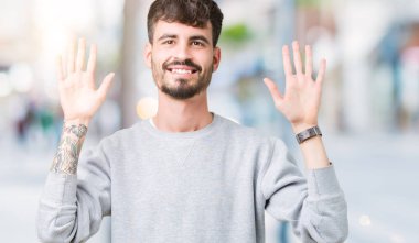 Gösterilen arka plan üzerinde sweatshirt giyen genç yakışıklı adam izole ve parmakları ile işaret kendinden emin ve mutlu gülümseyerek süre on numara.