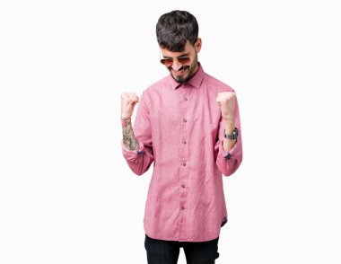 Yakışıklı delikanlı üzerinde güneş gözlüğü takıyor arka plan çok mutlu ve heyecanlı kaldırdı, silah ile kazanan jest yapıyor gülümseyen ve başarı için çığlık izole. Kutlama kavramı.