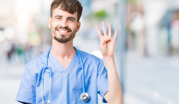 年轻英俊的护士男子穿着外科医生制服在孤立的背景显示和手指第四 同时微笑着自信和快乐 — 图库照片