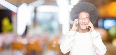 Afrikalı-Amerikalı genç afro saçlı kulakları ile yüksek sesle müzik gürültü rahatsız ifade parmaklarıyla kapsayan kış kazak giyiyor. Sağır kavramı.