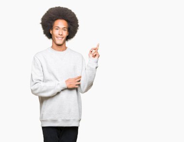 Yüzünde, kocaman bir gülümseme ile sportif sweatshirt giyen afro saçlı genç Afro-Amerikan adam kameraya bakarak yan el ve parmak ile işaret.