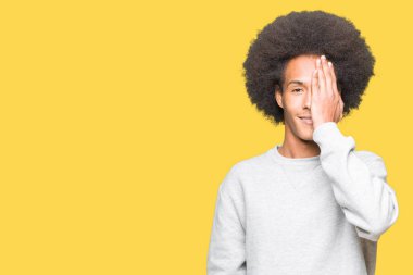 El yüz ve sürpriz duygu kendinden emin gülümseme ile tek gözüyle kapsayan sportif sweatshirt giyen afro saçlı genç Afro-Amerikan adam.