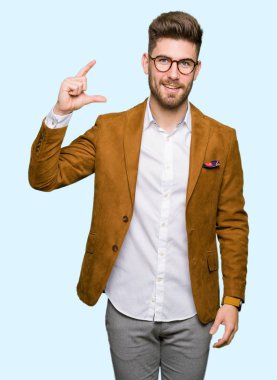 Gülümseyen bardakları ve boyutu işaret parmaklı ararken ve kamera işi el ile kendine güvenen el hareketi giyen genç yakışıklı iş adam. Ölçü kavramı.