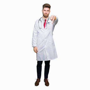 Genç yakışıklı Doktor adam mutsuz ve öfkeli gösteren reddetme ve başparmak aşağı jest ile negatif görünümlü tıbbi ceket giyiyor. Kötü ifade.