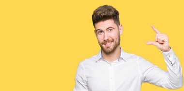 Gülümseyen genç yakışıklı iş adamı ve süre seyir ve kamera boyutu işaret parmaklarıyla yapıyor el ile kendine güvenen el hareketi. Ölçü kavramı.