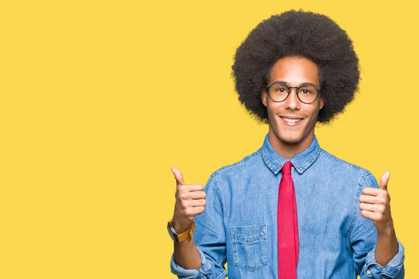 Young african american business man with afro hair wearing glasses and red tie success sign doing positive gesture with hand, thumbs up smiling and happy. Looking at the camera with cheerful expression, winner gesture.