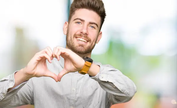 若いハンサムな男性がハートマークと手で形を示す愛の笑顔のカジュアルなシャツを身に着けています ロマンチックな概念 — ストック写真