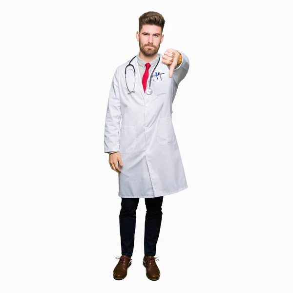 年轻英俊的医生男子穿着医疗外套看起来不高兴和愤怒 表现出拒绝和消极的大拇指向下的姿态 错误的表达 — 图库照片